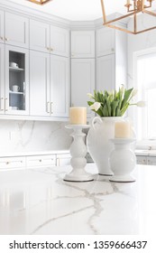 Elegant Table Decoration Of A Luxurious Custom Kitchen, With Marble Looking Quartz Countertop & Backsplash, As Well As Grey Cabinetry With Gold Accents. Beautifully Staged With Flowers And Candles.