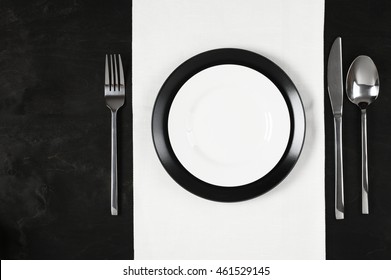 Elegant Table Setting: Black And White Plates With White Linen And Silverware On Black Wooden Table. Top View Point.