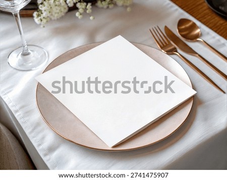 Elegant table setting with blank white menu card on rose gold charger plate, gold cutlery, wine glass, white linen and soft flowers; upscale wedding or event dining mockup with copy space.