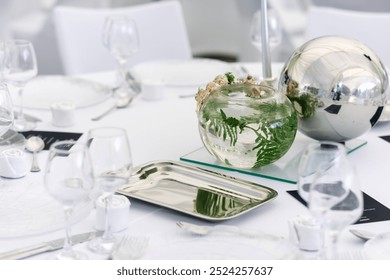 Elegant table setting featuring a glass vase with greenery and a decorative metal orb at a sophisticated dining event - Powered by Shutterstock