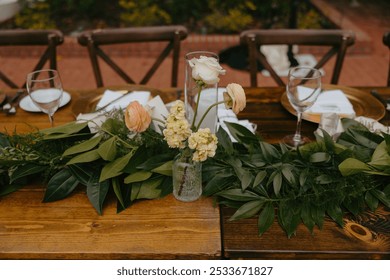 An elegant table setting with floral centerpiece and greenery at an outdoor event - Powered by Shutterstock