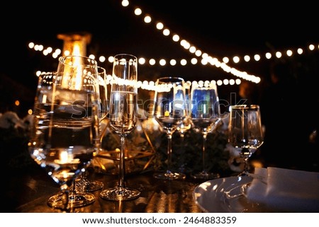 Elegant table setting with glasses and string lights at a night event.