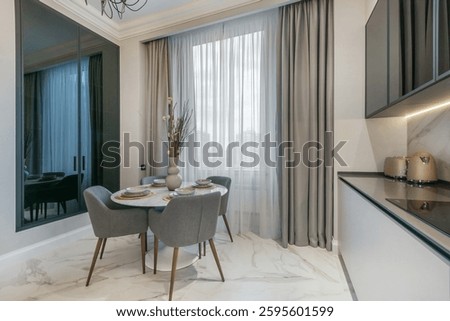 Elegant table setting in the interior of a modern kitchen. Built-in wardrobe with dark glass doors, window with beautiful drapery.