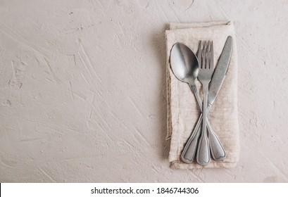 Elegant table setting: napkin and silverware on gray concrete background. Flat lay. Top view.