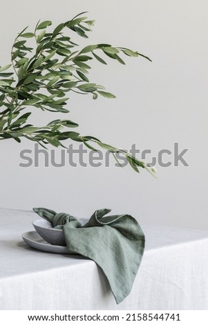 Elegant table setting with olive tree brunch in craft vase on linen tablecloth. Outdoor table setting for summer holiday concept.