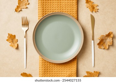 Elegant table setting with a pastel green plate on a textured yellow cloth, surrounded by dried autumn leaves. Ideal for fall decor, dining themes, and minimalist designs. - Powered by Shutterstock