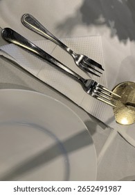 Elegant table setting with two forks on a napkin, beside a white plate and floral centerpiece.
