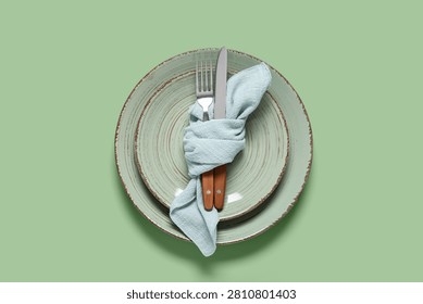 Elegant table setting with two rustic green plates, light blue napkin, and wooden handle cutlery on a solid green background