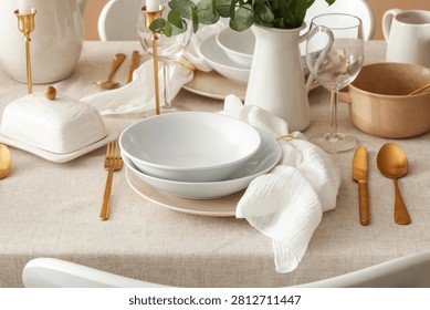 Elegant table setting with white ceramic dinnerware, gold cutlery, and eucalyptus decor for a special occasion