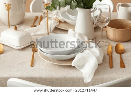 Elegant table setting with white ceramic dinnerware, gold cutlery, and eucalyptus decor for a special occasion