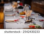 Elegant table setting with wine glasses, breadsticks, and plates on a white tablecloth, ready for a meal in a warm and inviting atmosphere.