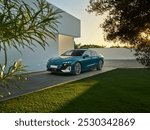 Elegant teal sedan parked in a modern home’s driveway, surrounded by lush greenery at sunset, showcasing the harmony between luxury, nature, and architecture.