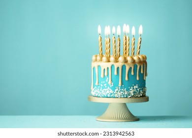 Elegant turquoise birthday cake with gold drip icing and gold birthday candles against a turquoise background