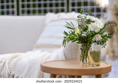 Elegant Vase Of Flowers And Candle In Focus Atop A Nice Wooden Table, With High End Furniture In The Background