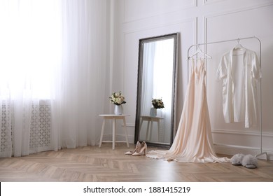 Elegant Wedding Dress And Silk Robe Hanging On Rack In Room