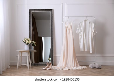 Elegant Wedding Dress And Silk Robe Hanging On Rack In Room