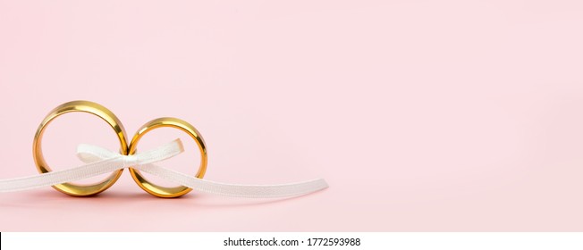 Elegant Wedding Or Engagement Banner Background - Pair Of Golden Wedding Rings And Gentle White Bow Ribbon On Gentle Pink Backdrop, Copy Space For Text