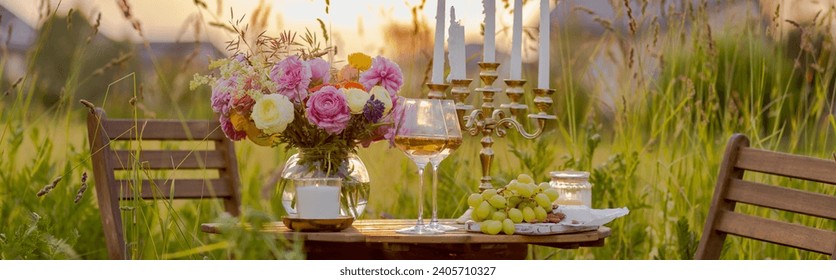 Elegant wedding or private party for a loving couple table setting outdoors in the garden. Beautiful decor with fresh ranunculi flowers, candles. Gourmet cheese board, fruits, white wine. Banner - Powered by Shutterstock