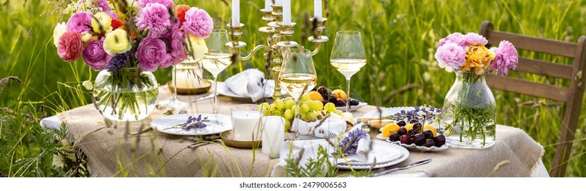 Elegant wedding or private party for a loving couple table setting outdoors in the garden. Beautiful decor with fresh ranunculi flowers, candles. Gourmet cheese board, fruits, white wine. Banner - Powered by Shutterstock