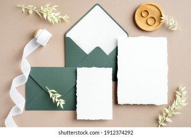 Elegant wedding stationery set. Wedding invitation cards templates, green envelopes, silk ribbon, golden rings on pastel beige background. Flat lay, top view, copy space.