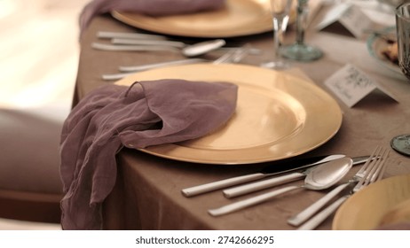 Elegant wedding table setting featuring a golden plate with a mauve gauzy napkin and silver cutlery