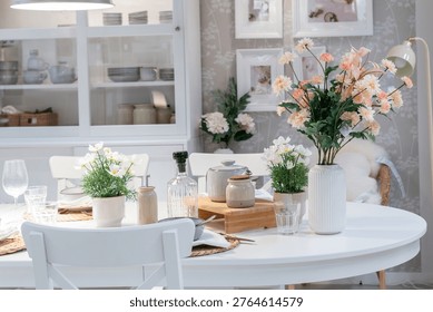 Elegant white dining table setting with fresh spring flowers and minimalist decor.Cozy bright dining room interior in Scandinavian style with floral centerpieces.