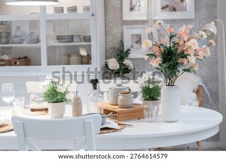 Elegant white dining table setting with fresh spring flowers and minimalist decor.Cozy bright dining room interior in Scandinavian style with floral centerpieces.