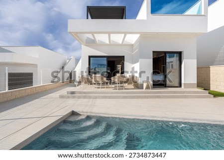 Elegant white facade with poolside seating, large windows, rooftop terrace, and open-air design