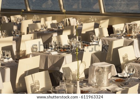 Elegant white place settings on a small dinner cruise boat with tables and chairs.
