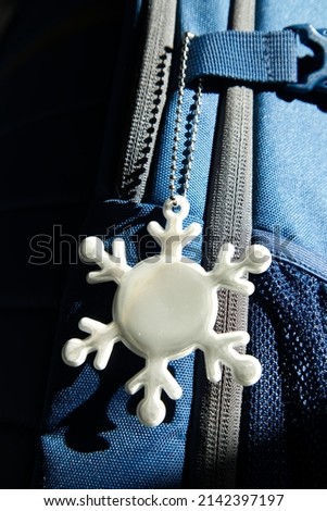 Elegant white reflective safety signal in a snow pattern form on a blue backpack for pedestrian visibility. Accessory essential for a walker or passerby to walk on the dark street.