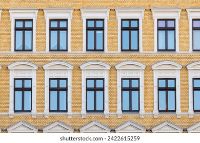 Elegant windows set facade vibrant yellow brick building, showcasing architectural symmetry and beautiful vintage windowsill stucco. Classic residential building front wall in european city center - Powered by Shutterstock