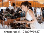 Elegant woman appreciating antiques, browsing with interest vintage glassware at local flea market, searching for unusual item to decorate home or gift..