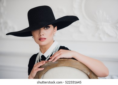 Elegant woman in black dress with a hat sitting on chair