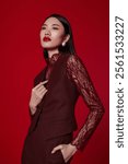 Elegant Woman in Burgundy Lace Outfit Posing Confidently Against a Bold Red Background – Sophisticated Fashion and Beauty Portrait.