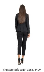 Elegant woman in business black suit walking away. Rear view. Full body length portrait isolated over white studio background. 