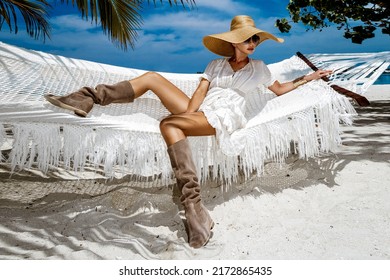 Elegant Woman In Fashionable Dress And Big Hat On Tropical Beach On Maldives Island. Summer Fashion. Female Model Is Posing On The Sandy Beach. Maldives Landscape. Luxury Travel.