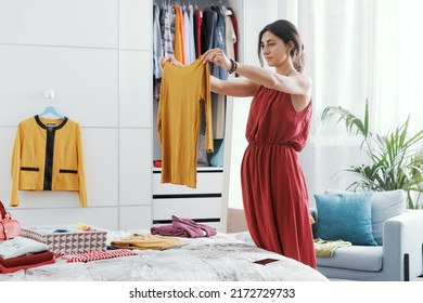 Elegant woman in her bedroom, she is decluttering her wardrobe and choosing clothes - Shutterstock ID 2172729733