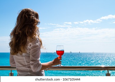 The elegant woman holding a glass of red wine with the background of a sunny seaside view.