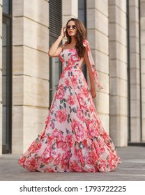 Elegant Woman In Long Pink Summer Dress With Floral Print Walking At City Street. Outdoor Full Length Portrait. Pretty Female Model