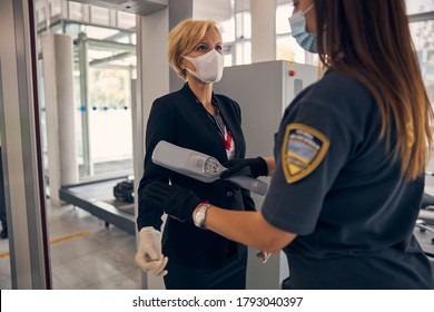 Elegant woman in medical face mask passing through metal detector scanner in airport terminal