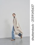 Elegant Woman in Minimalist Beige Coat, Turtleneck, and Jeans Striding Confidently in Modern Studio Setting - Fashion and Lifestyle Concept