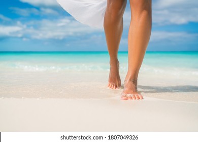 Elegant woman on luxury Caribbean beach vacation relaxing in summer tropical ocean background. Relax feet and legs walking enjoying sun tan lifestyle.