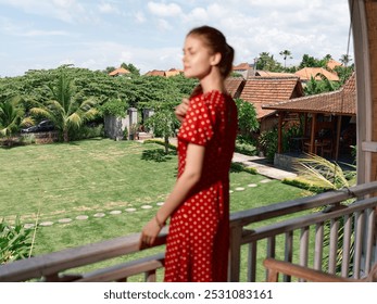 Elegant woman in red polka dot dress admiring scenic view from balcony on sunny day - Powered by Shutterstock