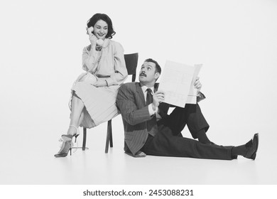 Elegant woman talking on retro phone and man sitting and reading newspaper. Monochrome image. Concept of retro and vintage, fashion, business, communication and lifestyle - Powered by Shutterstock