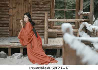 Elegant Woman in Traditional Asian Attire Sitting Outside a Rustic Wooden Cabin in a Serene Snow-Covered Winter Landscape. - Powered by Shutterstock