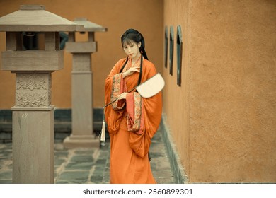 Elegant Woman in Traditional Orange Hanfu Holding a Fan in a Historic Courtyard Setting, Showcasing Timeless Chinese Culture and Grace. - Powered by Shutterstock