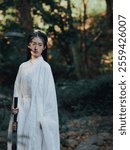 Elegant Woman in Traditional White Robe Holding Sword in Serene Forest Setting – Timeless Beauty and Grace in Nature.