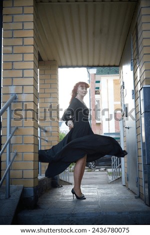 Elegant Woman Twirling in Black Dress on Staircase. A woman in a twirling black dress captured mid-movement on the porch of the house