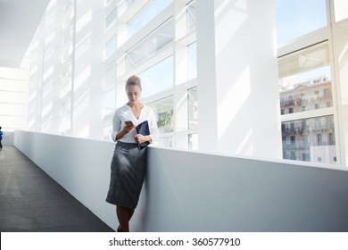 Elegant woman using mobile phone after work on digital tablet while standing in office interior,female manager read text message on cell telephone while waiting for her colleague after finish work day - Powered by Shutterstock