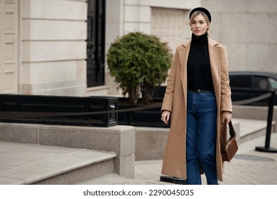Elegant woman walking street in fashionable spring or autumn clothes cashmere double breasted coat, black turtleneck, jeans and small bag. Female model in motion, street style fashion - Shutterstock ID 2290045035